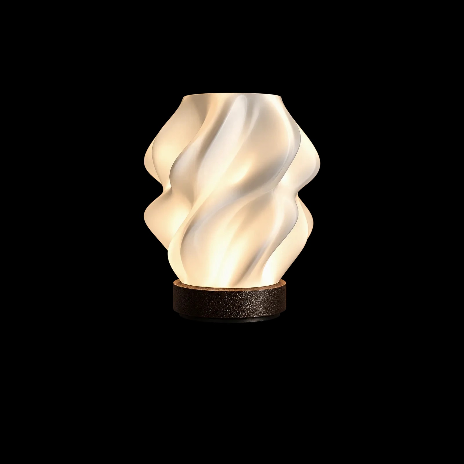 Curva 01 encendida: una pantalla blanca que se tuerce en pliegues suaves, iluminada desde adentro, sobre una base circular de madera oscura.